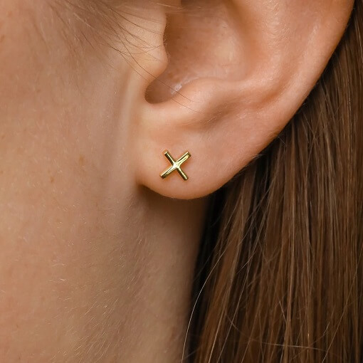 Model wearing tiny, minimal sterling silver plated in gold cross nought studs
