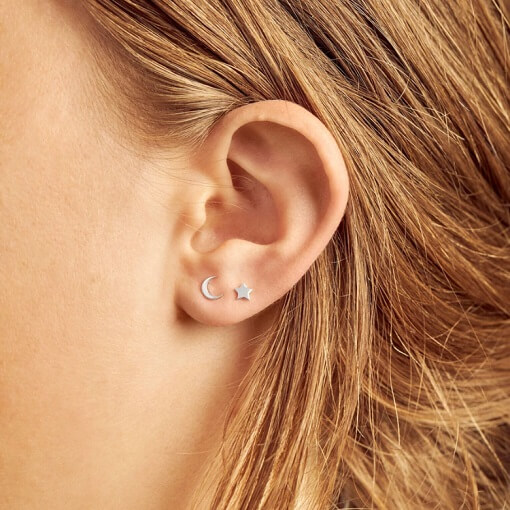 model wearing tiny, minimal sterling silver star and moon studs