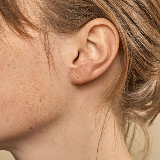 Model wearing tiny, minimal sterling silver, gold plated star studs